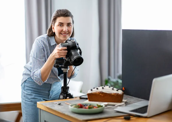 blogging, profession and people concept - happy smiling female food photographer with camera photographing cake in kitchen at home