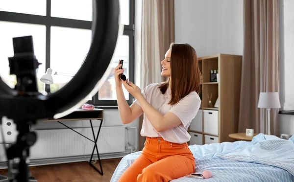 beauty blogging, technology and people concept - happy smiling girl blogger with ring light and smartphone applying make up at home