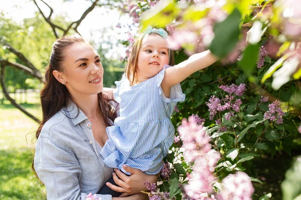 母性和人的概念 快乐的母亲带着小女儿在夏季公园或花园触摸紫丁香花 — 图库照片