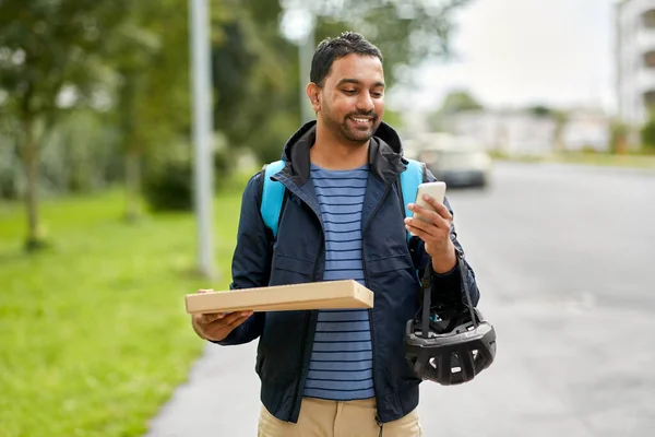 food shipping, profession and people concept - happy smiling delivery man with thermal insulated bag and takeaway pizza box using smartphone on city street