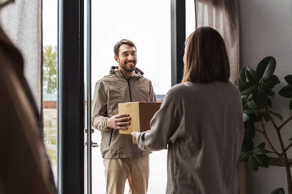 shipping, transportation and people concept - delivery man with parcel box and customer at home