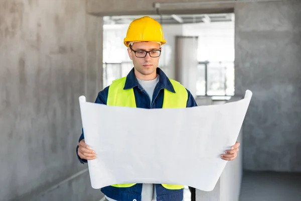 architecture, construction business and people concept - male architect in helmet with blueprint at office