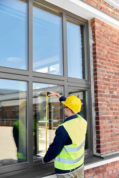 construction business and building concept - male builder with ruler measuring window