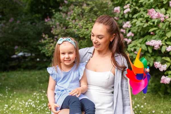 母性和人的概念 快乐的母亲带着小女儿在夏季公园或花园玩别针轮玩具 — 图库照片