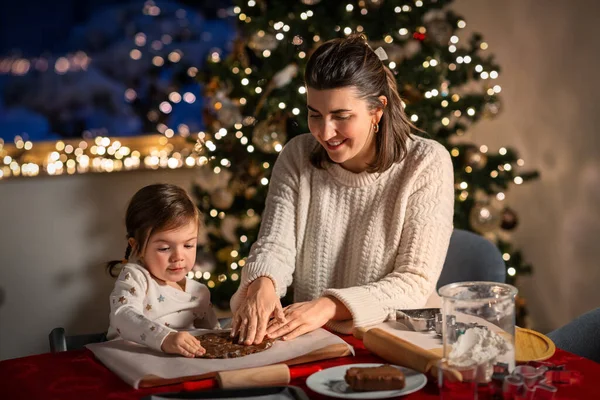 family, cooking and winter holidays concept - happy mother and baby daughter having fun with dough for gingerbread cookies at home on christmas