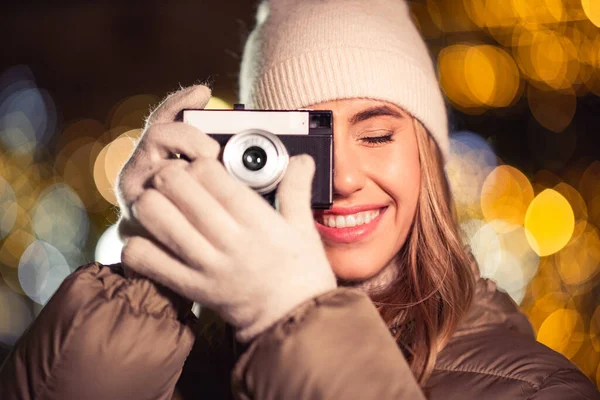 winter holidays, photography and people concept - happy smiling woman with film camera over christmas lights in evening