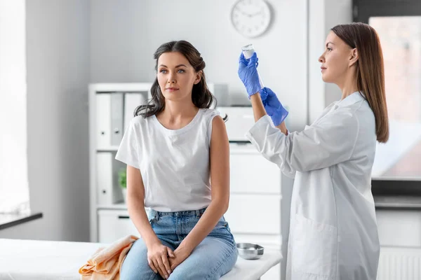 health, medicine and pandemic concept - smiling female doctor or nurse wearing protective medical gloves with syringe vaccinating patient at hospital