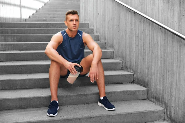 フィットネス スポーツ 人々のコンセプト 疲れた若い男とタンパク質が階段に座ってボトルを振る — ストック写真