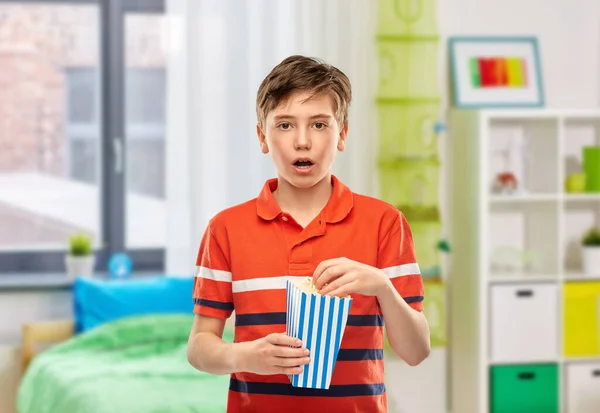 movie theater, cinema and people concept - portrait of boy eating popcorn from striped bucket over home room background