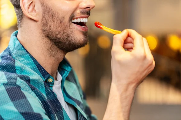 fast food and people concept - close up of happy man eating french fries with ketchup at restaurant
