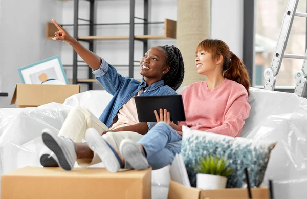 moving, people and real estate concept - happy smiling women with tablet pc computer and boxes making plans at new home