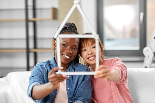 moving, people and real estate concept - happy smiling women with ruler folded in shape of house at new home