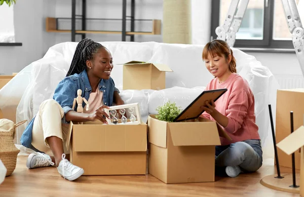 moving, people and real estate concept - women unpacking boxes at new home