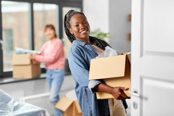 moving, people and real estate concept - happy smiling women with boxes at new home