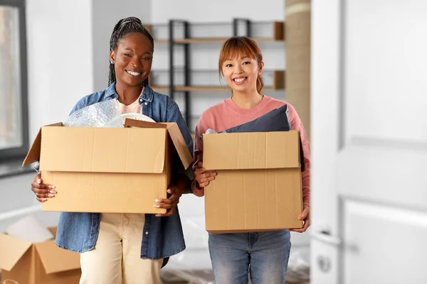 moving, people and real estate concept - happy smiling women with boxes at new home