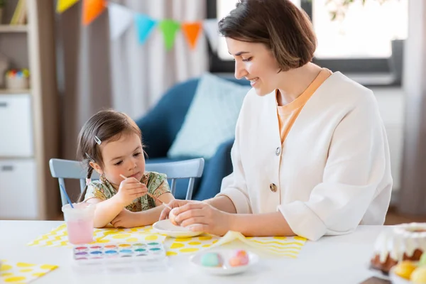holidays, family and people concept - happy mother and little baby daughter coloring easter eggs with watercolors at home