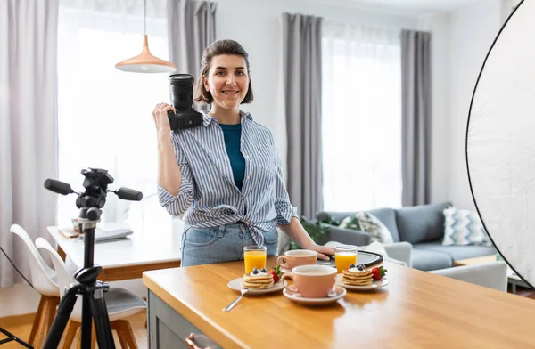 blogging, profession and people concept - happy smiling female food photographer with camera photographing pancakes, coffee and orange juice in kitchen at home