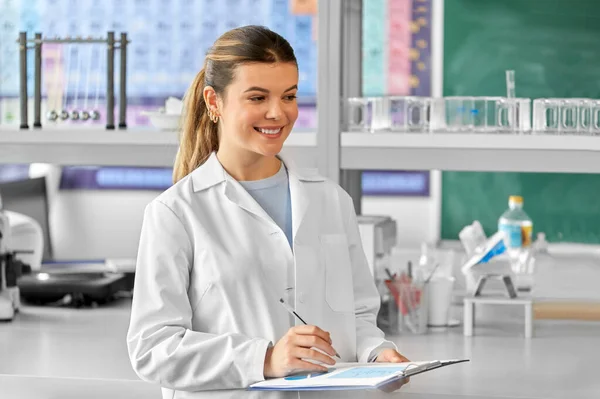 science, work and people concept - happy smiling female scientist with clipboard working in laboratory