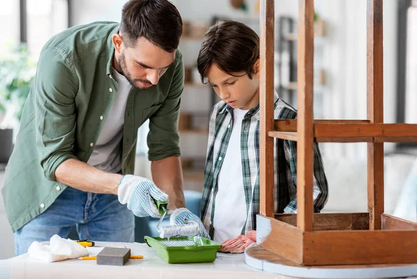 renovation, diy and home improvement concept - father and son in gloves with paint roller painting old wooden table in grey color