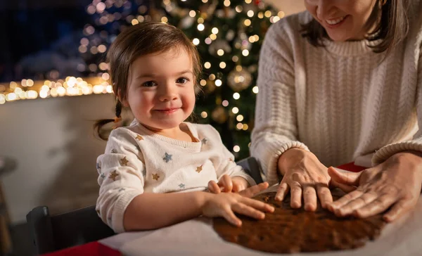 family, cooking and winter holidays concept - happy mother and baby daughter having fun with dough for gingerbread cookies at home on christmas