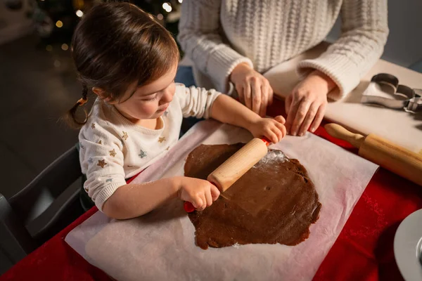 family, cooking and winter holidays concept - happy mother and baby daughter with rolling pin making gingerbread cookies from dough at home on christmas