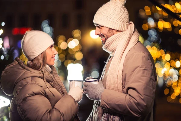 people, holidays and leisure concept - happy couple with tea cups over christmas lights