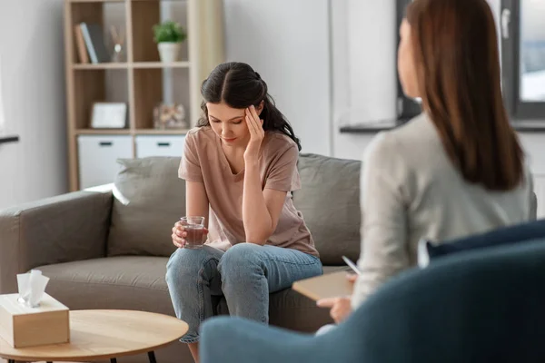 psychology, mental health and people concept - sad young woman patient with glass of water and woman psychologist at psychotherapy session