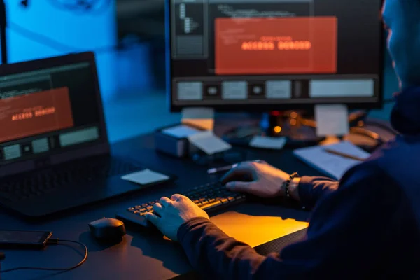 cybercrime, hacking and technology concept - close up of male hacker in dark room writing code or using computer virus program for cyber attack