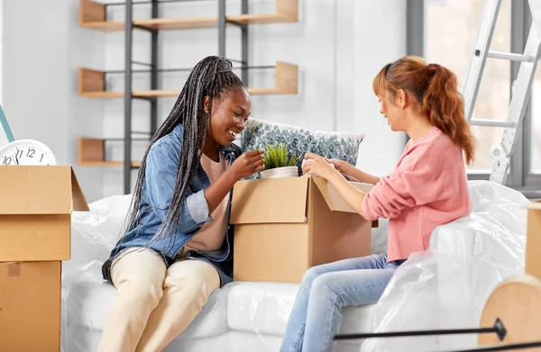 moving, people and real estate concept - women unpacking boxes at new home