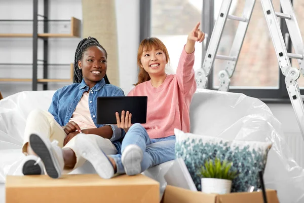 moving, people and real estate concept - happy smiling women with tablet pc computer and boxes making plans at new home