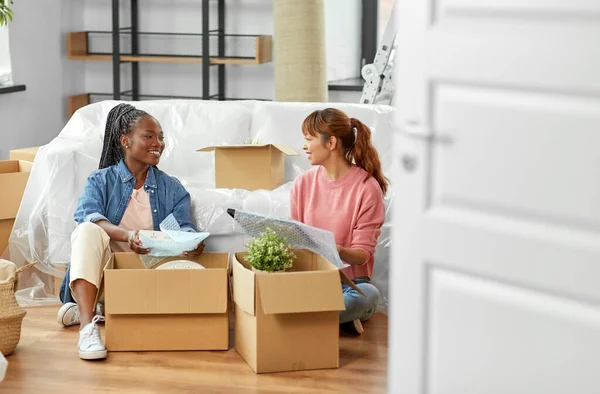 moving, people and real estate concept - women unpacking boxes at new home or packing stuff into bubble wrap