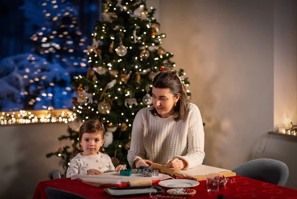 family, cooking and winter holidays concept - happy mother and baby daughter making gingerbread cookies at home on christmas