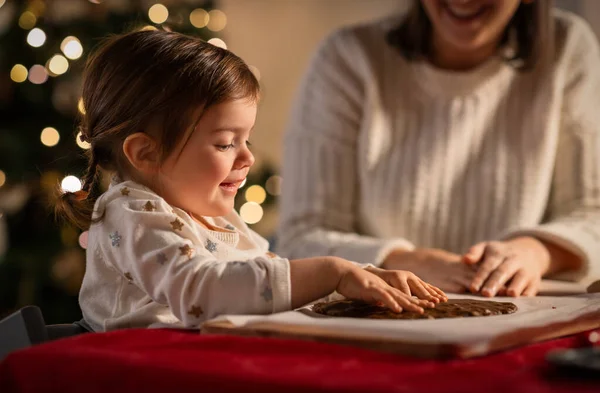 family, cooking and winter holidays concept - happy mother and baby daughter having fun with dough for gingerbread cookies at home on christmas