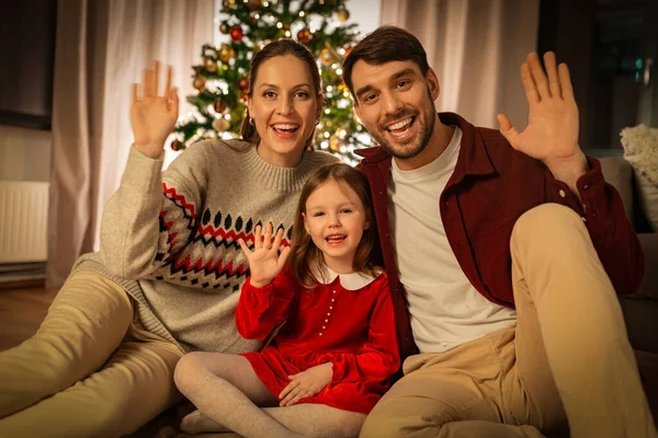 winter holidays, family and christmas concept - happy mother, father and little daughter waving hand at home