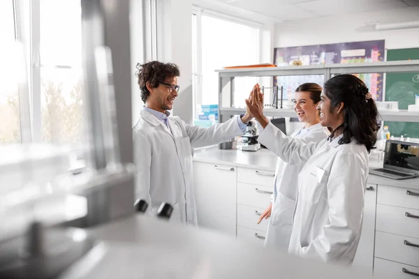 science, work and people concept - international group of happy scientists making high five gesture in laboratory