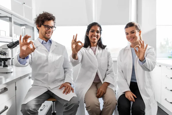 science, work and people concept - international group of happy scientists in laboratory showing ok gesture