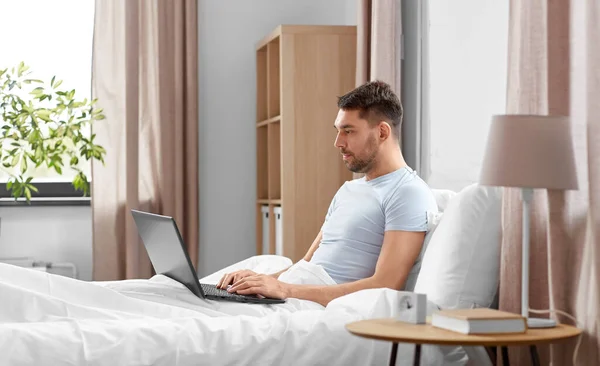 人と技術とリモートの仕事の概念 ラップトップコンピュータを持つ男が自宅のベッドルームに横たわっている — ストック写真