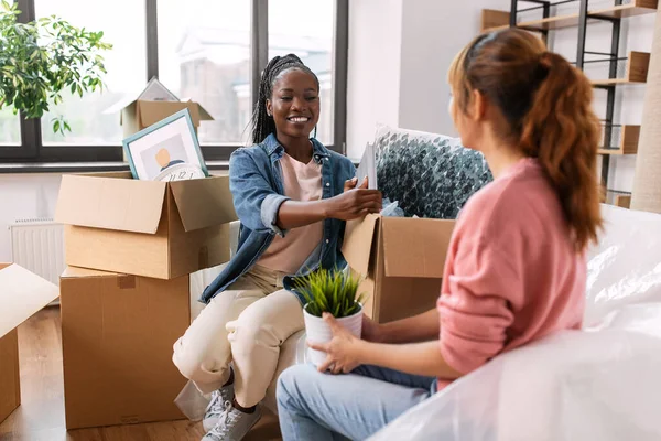 moving, people and real estate concept - happy smiling women unpacking boxes at new home