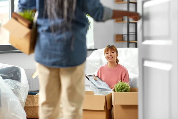 moving, people and real estate concept - woman unpacking boxes at new home and her friend entering room