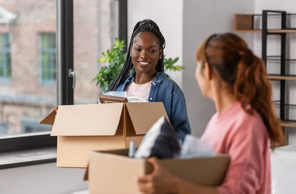 moving, people and real estate concept - happy smiling women with boxes at new home