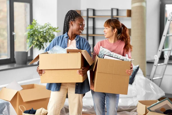 moving, people and real estate concept - happy smiling women with boxes at new home