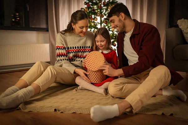 winter holidays, family and celebration concept - happy mother, father and little daughter opening christmas gift at home