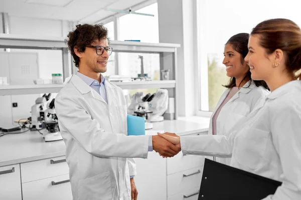 science, work and people concept - international group of happy scientists shaking hands in laboratory