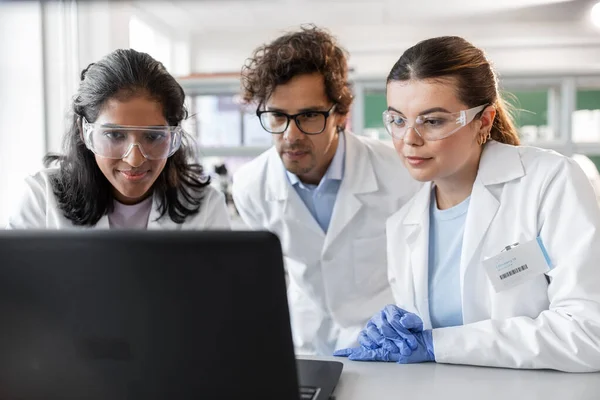 science research, work and people concept - international team of scientists with laptop computer working in laboratory