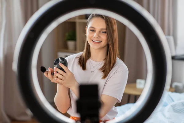 beauty blogging, technology and people concept - happy smiling girl blogger with ring light and smartphone applying make up at home