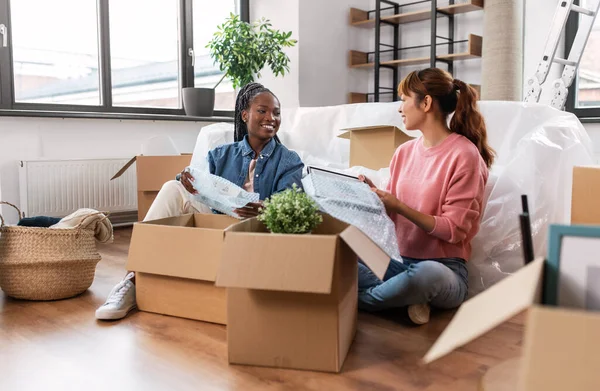 moving, people and real estate concept - happy smiling women packing or unpacking boxes at home