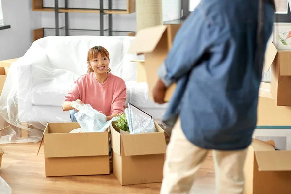moving, people and real estate concept - women unpacking boxes at new home