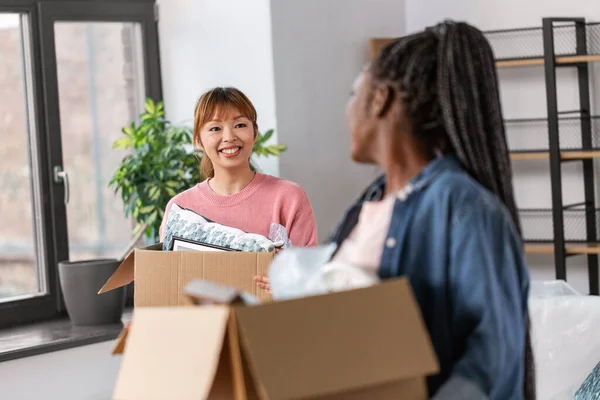 moving, people and real estate concept - happy smiling women with boxes at new home