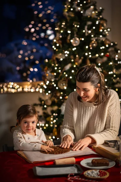 family, cooking and winter holidays concept - happy mother and baby daughter having fun with dough for gingerbread cookies at home on christmas