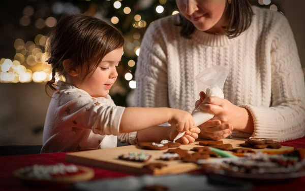 冬の休暇のコンセプト クリスマスに家でジンジャーブレッドクッキーを飾るベーキングバッグでアイシングを持つ幸せな母親と赤ちゃんの娘 — ストック写真